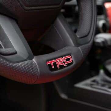 Close-up of the Toyota TRD steering wheel, featuring textured grip and TRD badge in red.