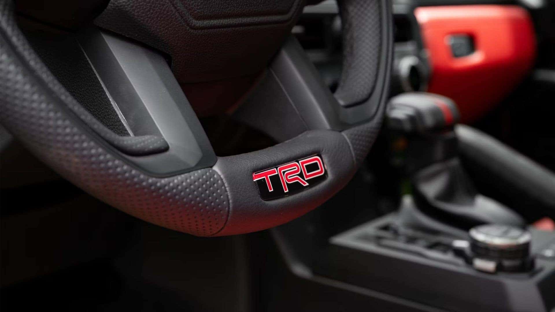 Close-up of the Toyota TRD steering wheel, featuring textured grip and TRD badge in red.