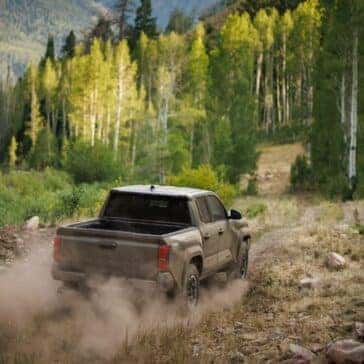 Toyota Tacoma driving through a lush forest trail, leaving a dust trail behind.