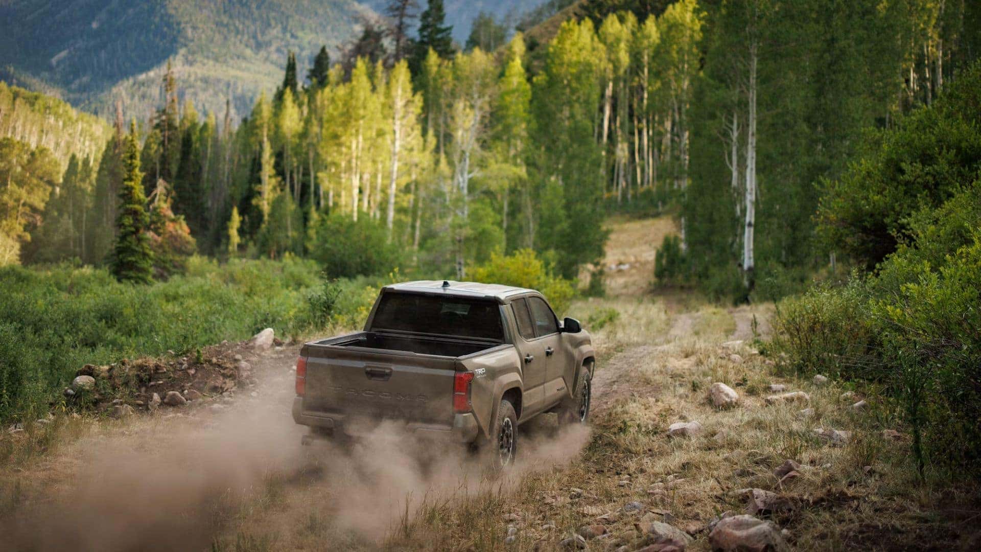 Toyota Tacoma driving through a lush forest trail, leaving a dust trail behind.