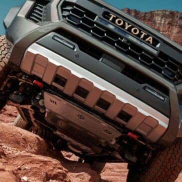 Close-up view of the Toyota Tacoma's underbody protection while navigating steep red rock terrain.