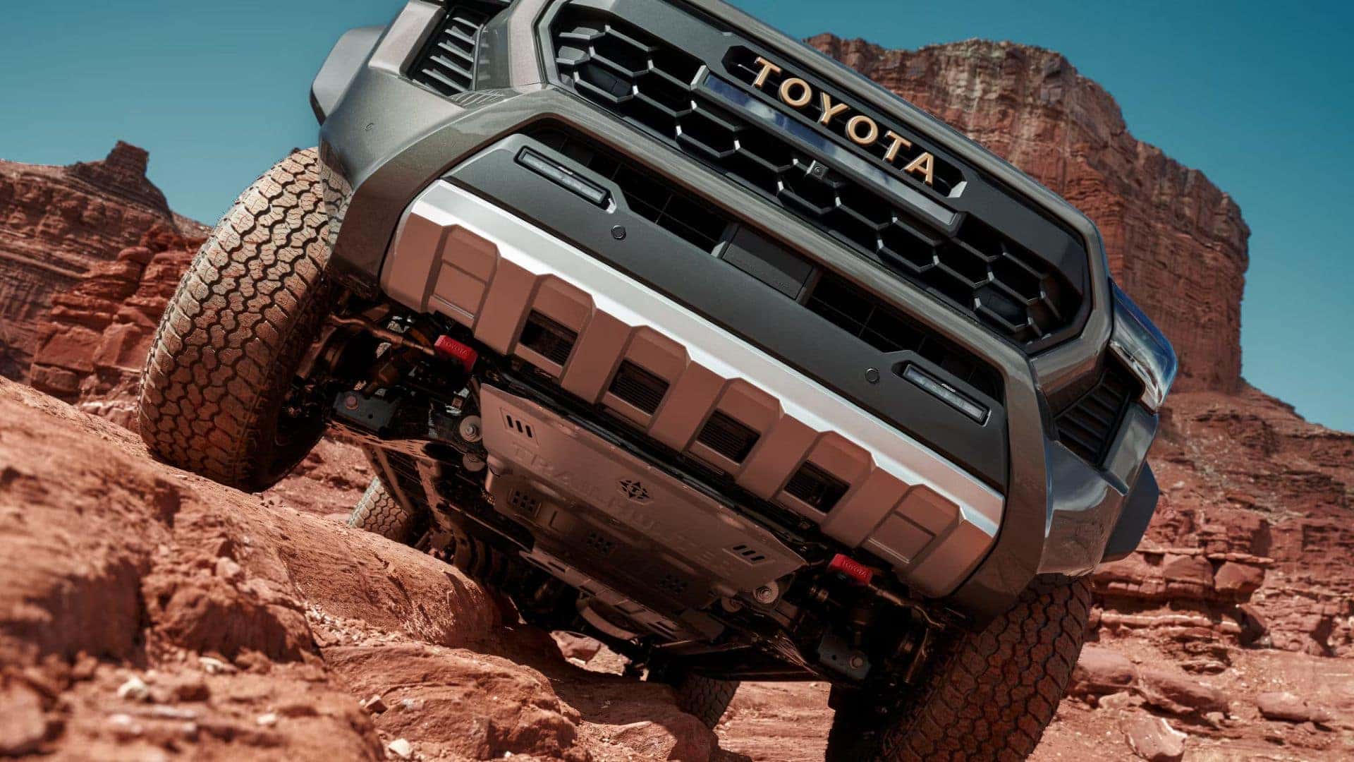 Close-up view of the Toyota Tacoma's underbody protection while navigating steep red rock terrain.