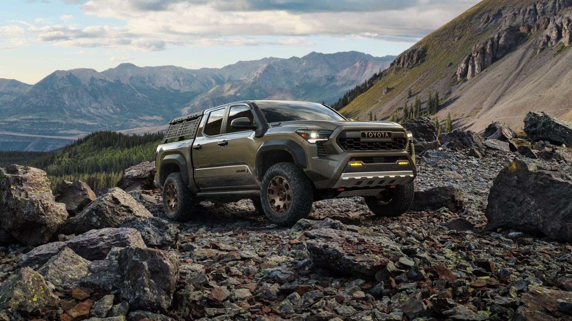 Toyota Tacoma parked on a rocky landscape with panoramic views of surrounding mountains and forests.