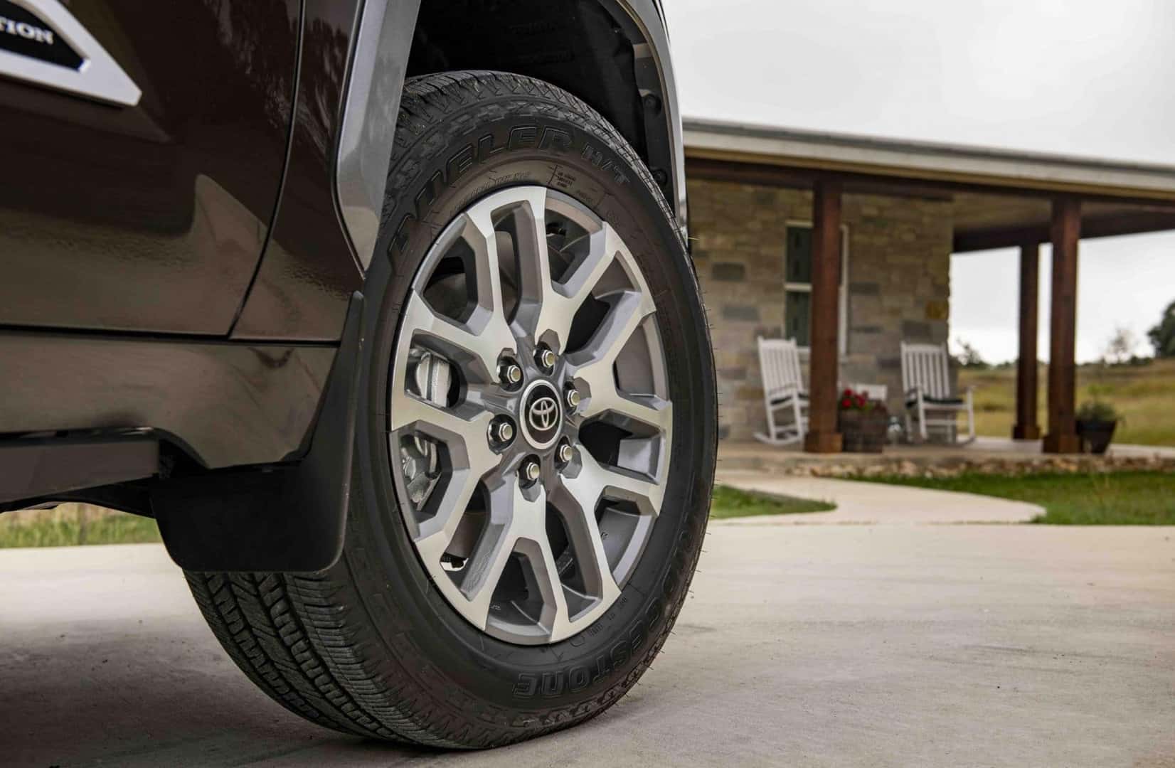 front passenger tire of a 2025 toyota tundra 1794 edition in smoked mesquite exterior paint with a house in the background