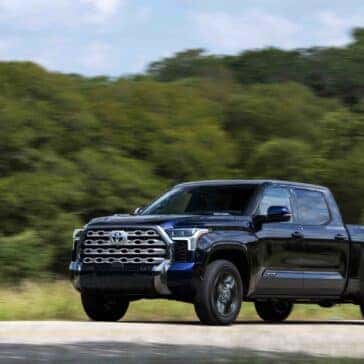 a blue toyota tundra truck driving on a road with a wooded background
