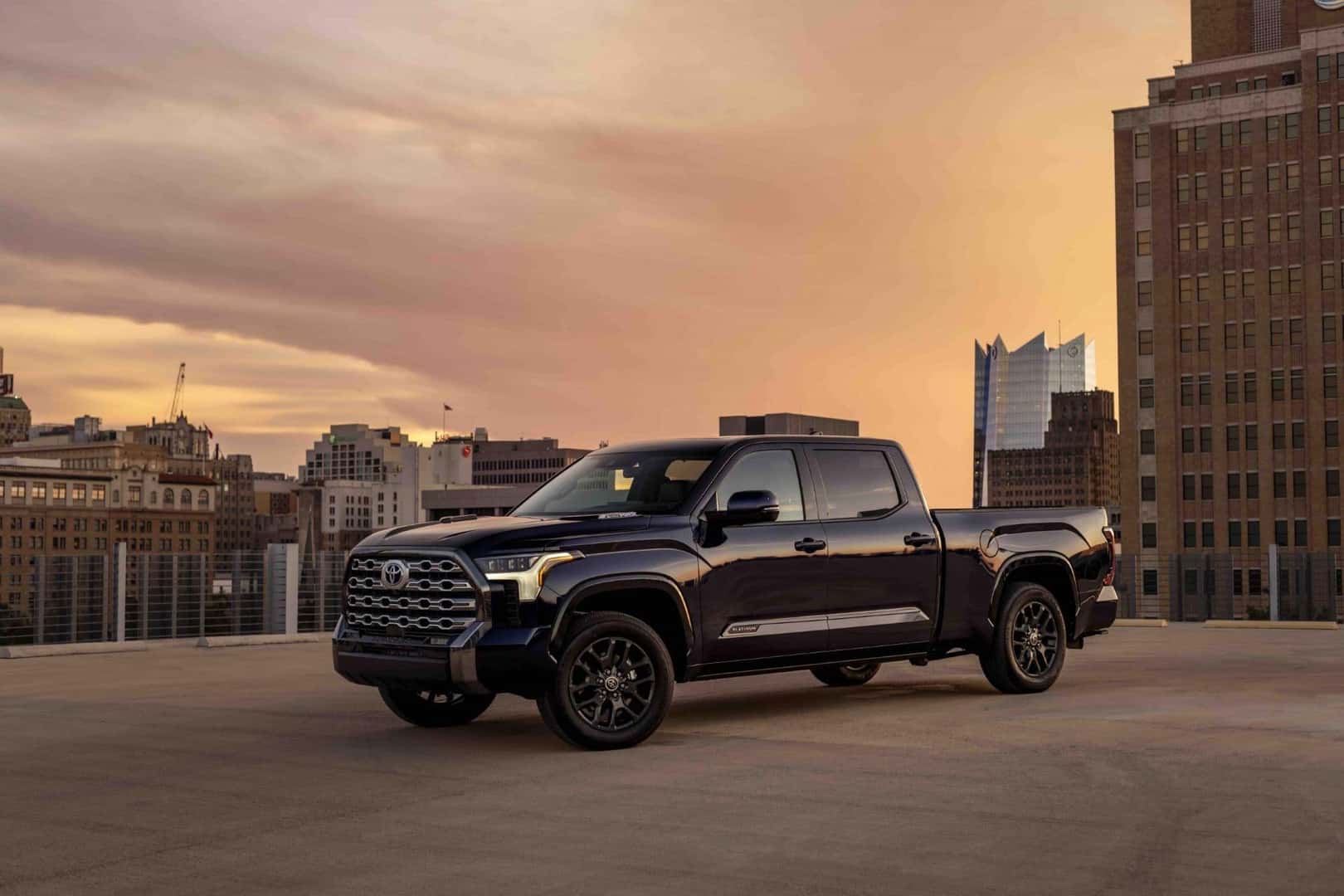 a blue truck parked on the top area of a parking garage showcasing city buildings at dusk