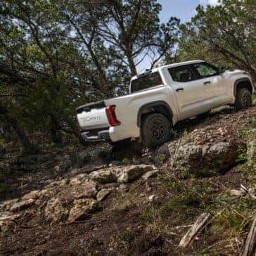 a white tundra TRD Pro driving up hill on a dirt path in the woods.