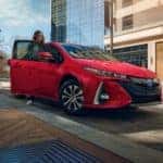 A couple is shown charging their red 2021 Toyota Prius Prime Limited on a side street.