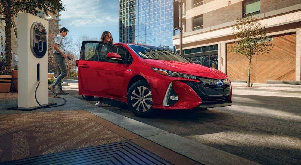 A couple is shown charging their red 2021 Toyota Prius Prime Limited on a side street.