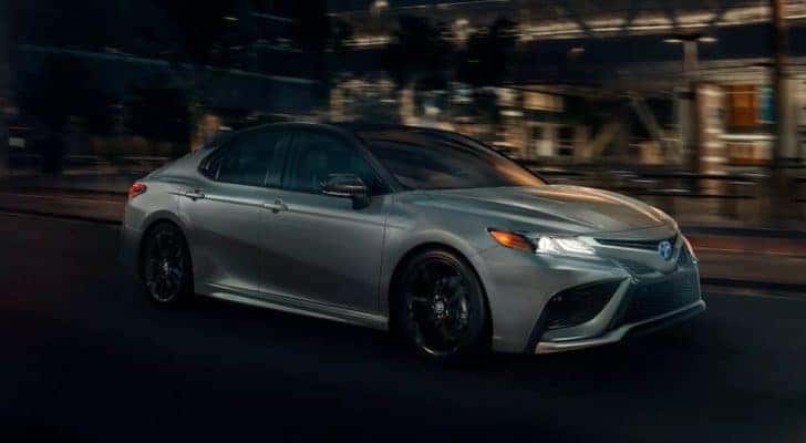 A silver 2022 Toyota Camry XSE Hybrid is shown driving through a city at night after visiting Toyota Camry dealer.