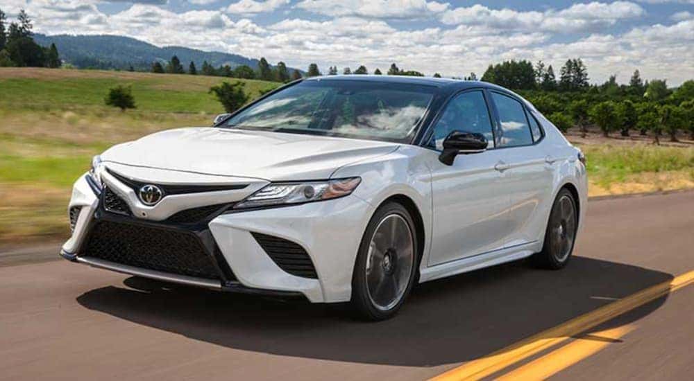 A white 2018 Toyota Camry is shown driving on an open road.