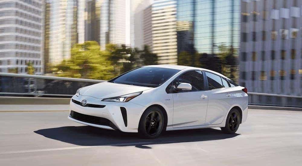 A white 2018 Toyota Prius is shown from the side while driving through the city after the owner searched 'used Toyota for sale'.