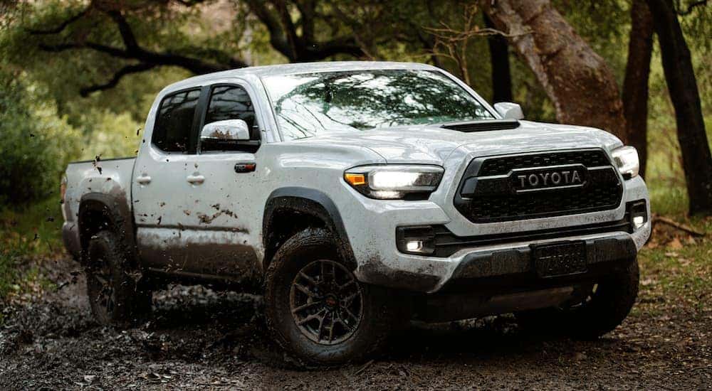 A white 2018 Toyota Tacoma is shown from the front at an angle while driving through mud.