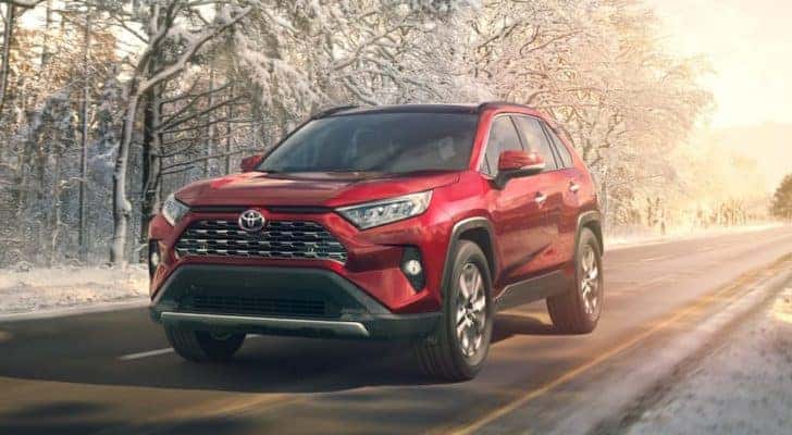 A popular used Toyota for sale, a red 2019 Toyota RAV4, is shown driving down a snowy road.