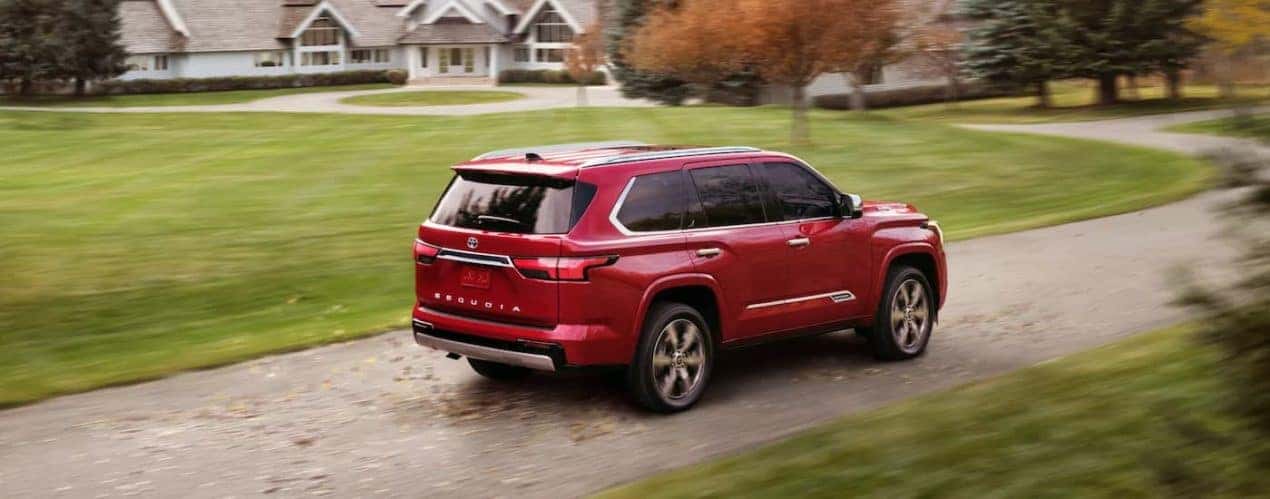 A red 2023 Toyota Sequoia is shown from a rear angle driving on a dirt road.