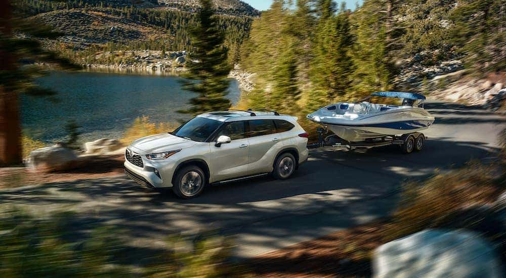 A white 2022 Toyota Highlander is shown from the side while towing a boat after leaving a Toyota Highlander dealer.