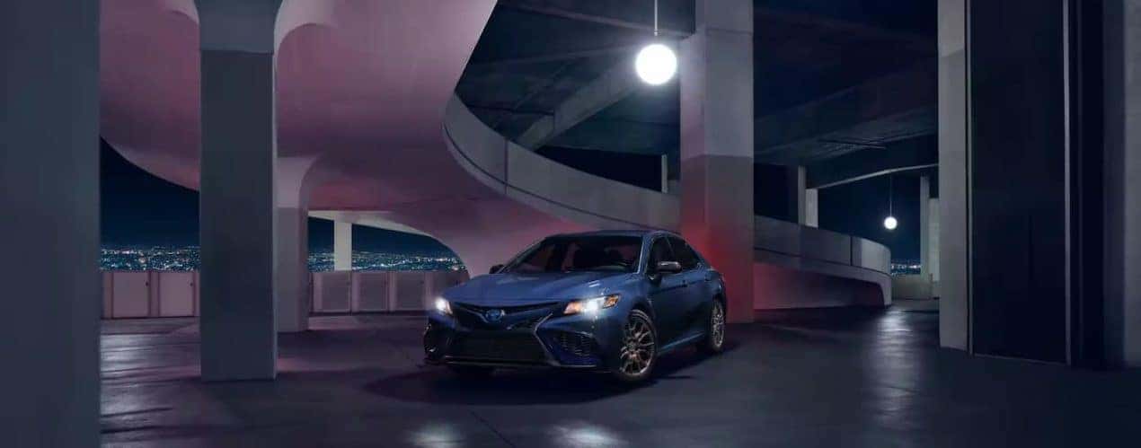 A blue 2023 Toyota Camry SE Hybrid Nightshade is shown driving through a parking garage.