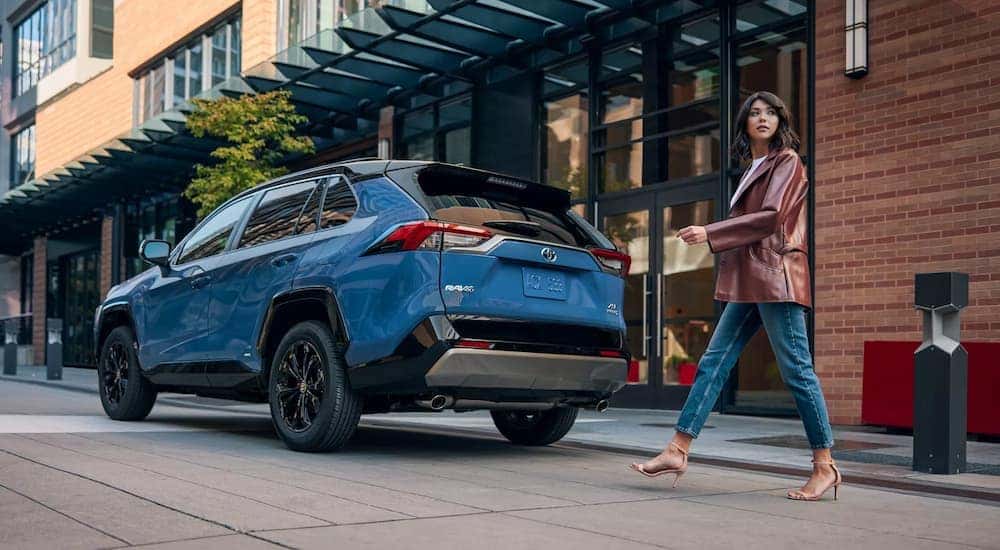 A woman is shown walking past a blue 2022 Toyota RAV4 XSE parked on a city street.