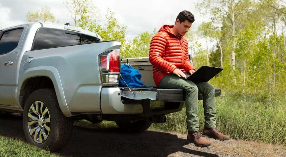 A person is shown using a laptop on the bad of a silver 2023 Toyota Tacoma Limited.