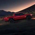 A red 2023 Toyota Tacoma SR5 SX for sale is shown from the side driving on a trail at night.