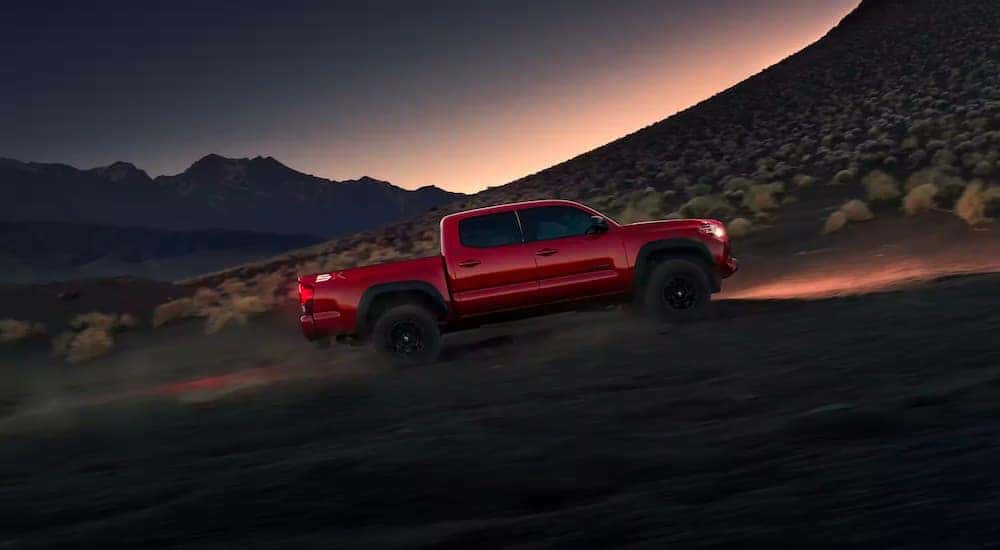 A red 2023 Toyota Tacoma SR5 SX for sale is shown from the side driving on a trail at night.