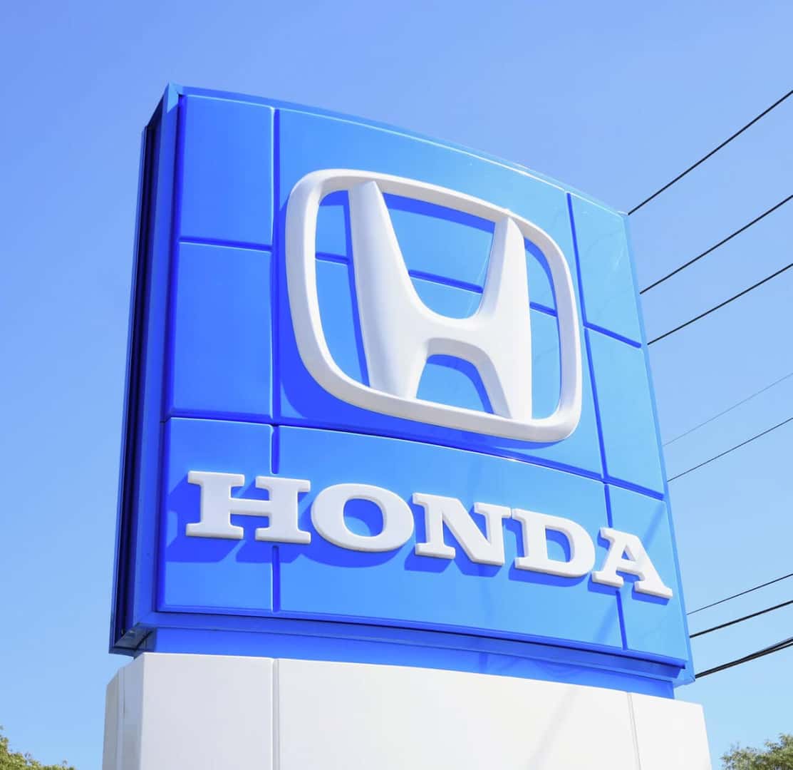 Exterior street view of a Honda dealership sign against a clear blue sky.