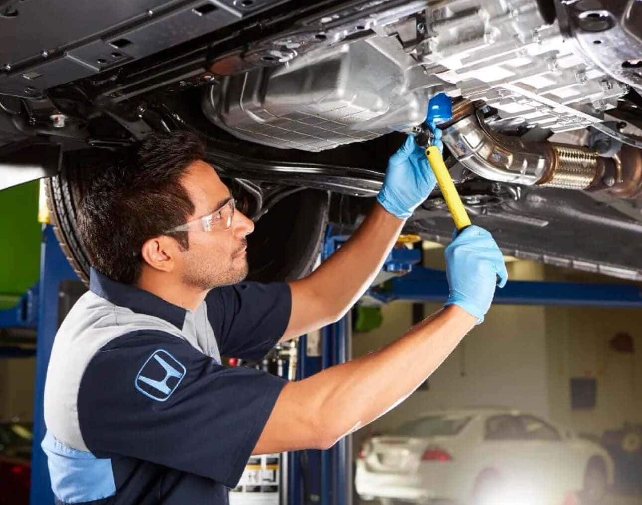 A service technician tightens a bolt under a raised Honda vehicle in a service center.
