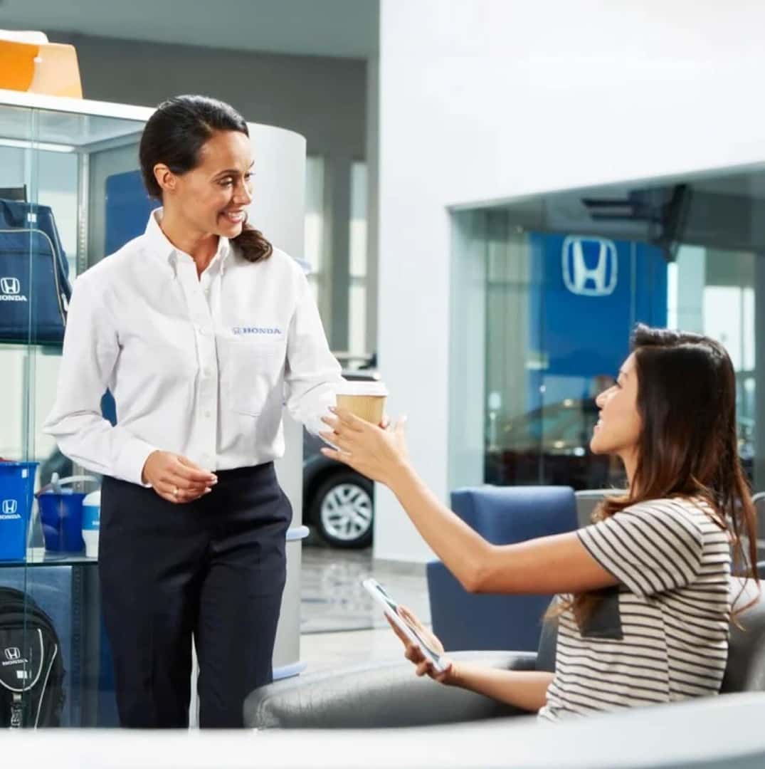 A service center representative hands a coffee too a custoer in a bright clean Honda dealership.