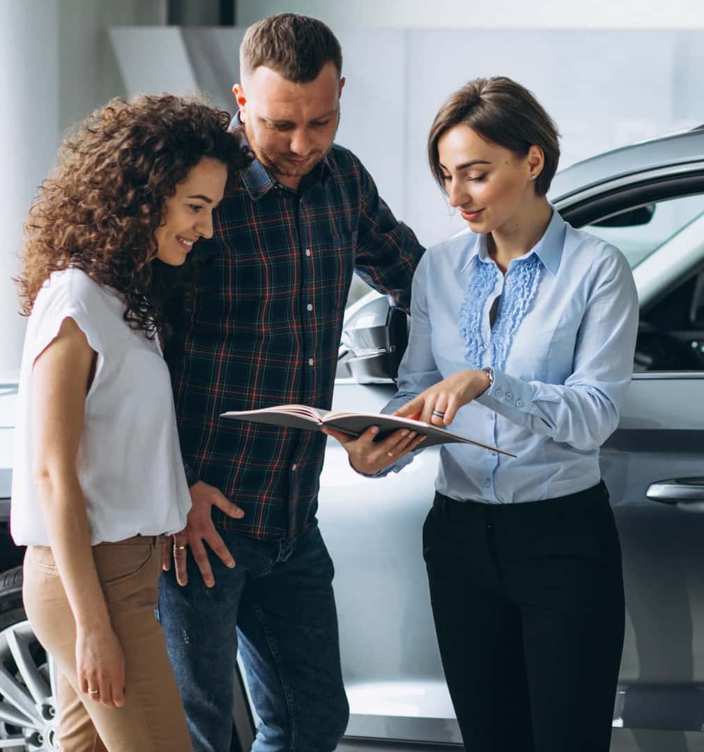 Couple reviewing vehicle information with a salesperson beside a car.