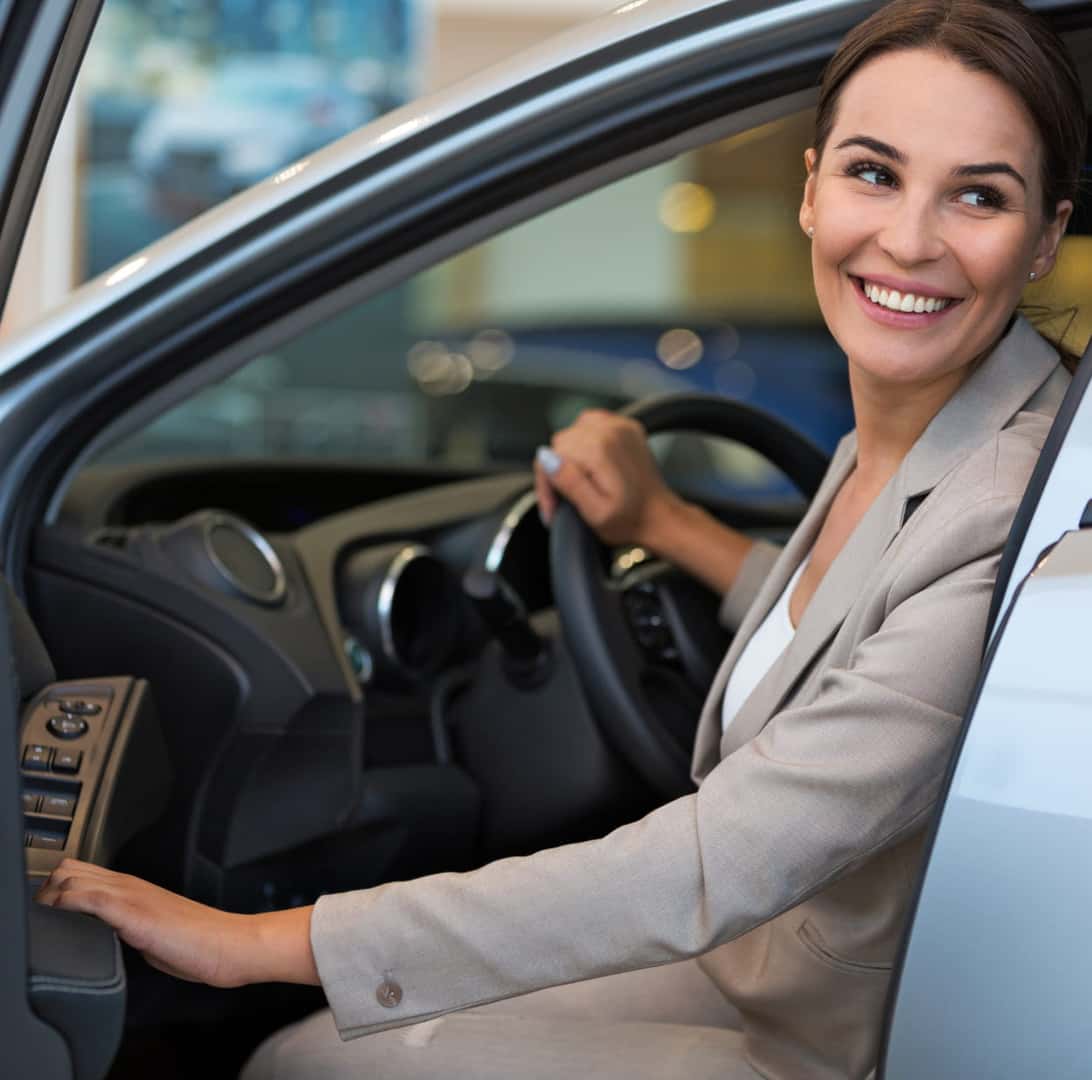 Smiling woman sitting in the driver’s seat of a vehicle.