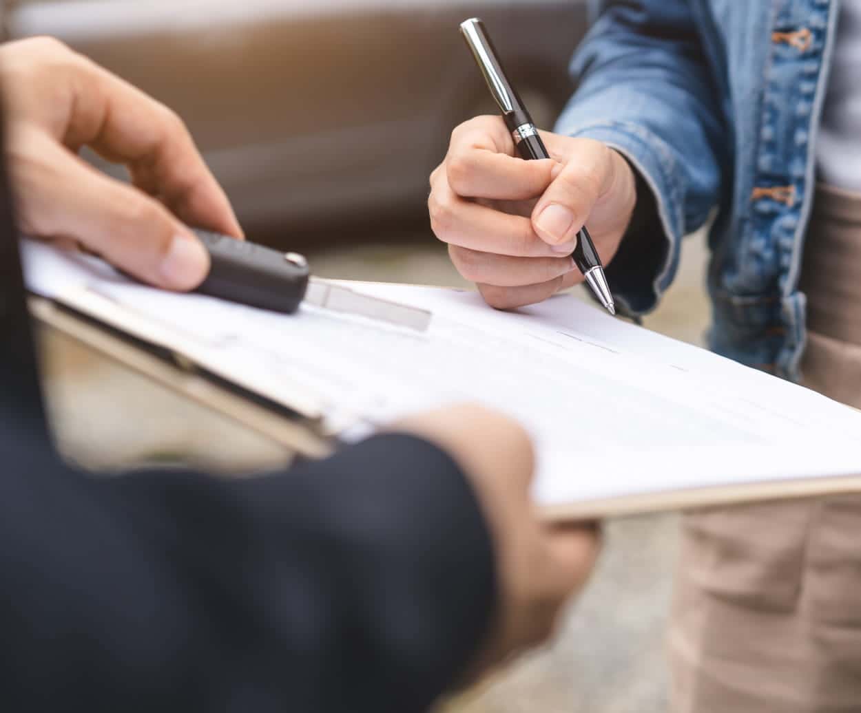 Customer holding a pen and car key while reviewing paperwork on a clipboard.
