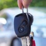 car keys dangle in the foreground and an out-of-focus car sits in the background