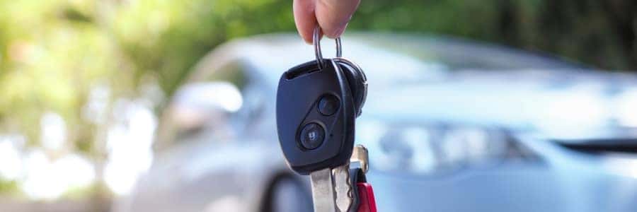 car keys dangle in the foreground and an out-of-focus car sits in the background