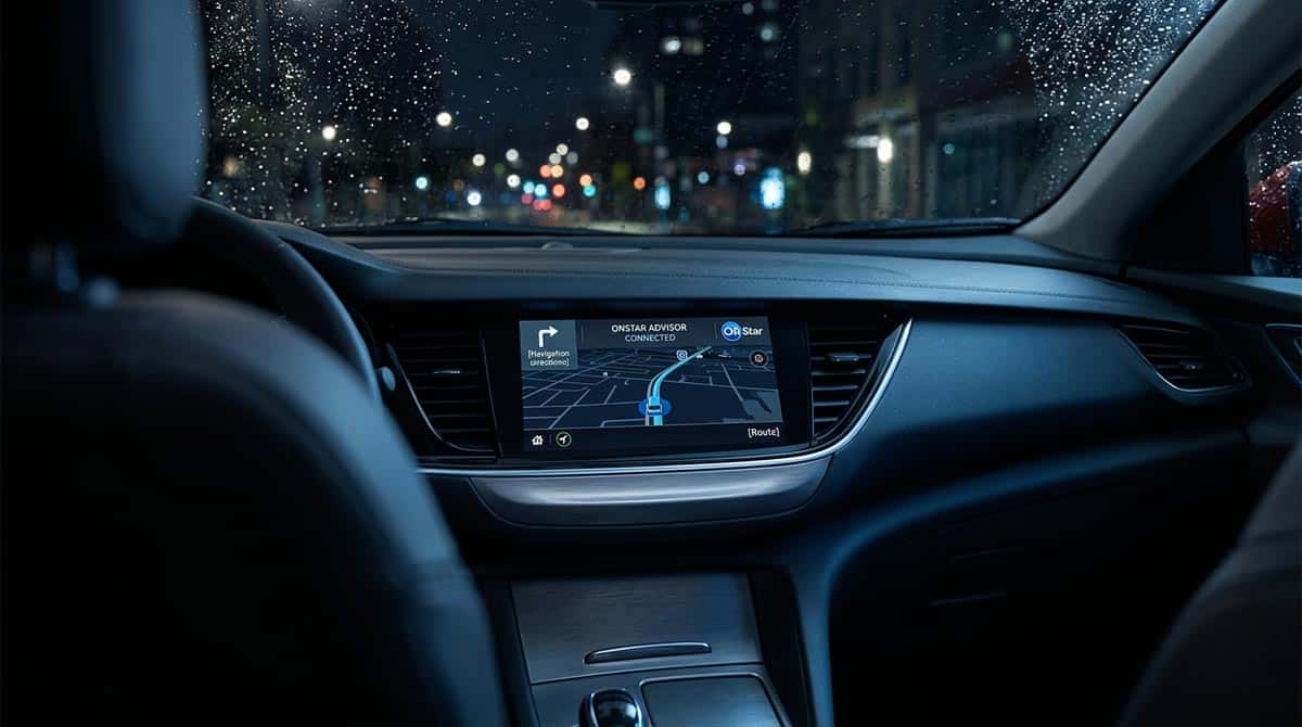 Modern vehicle interior screen showing OnStar navigation interface, dramatic blue ambient lighting, rainy night outside the windshield